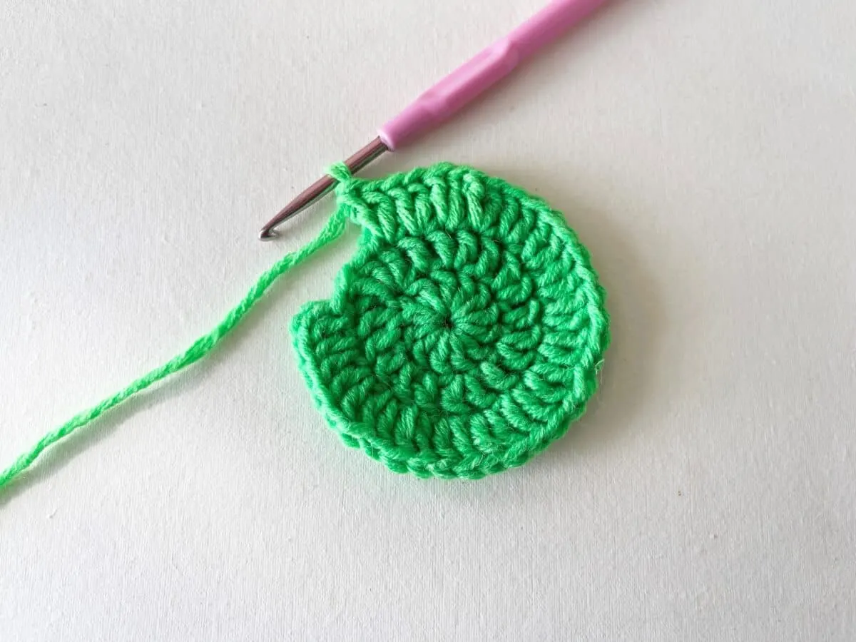 A green crocheted circle with a pink crochet hook.