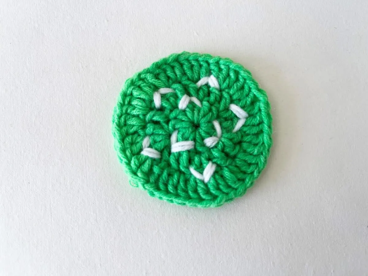 A green crocheted flower on a white surface.