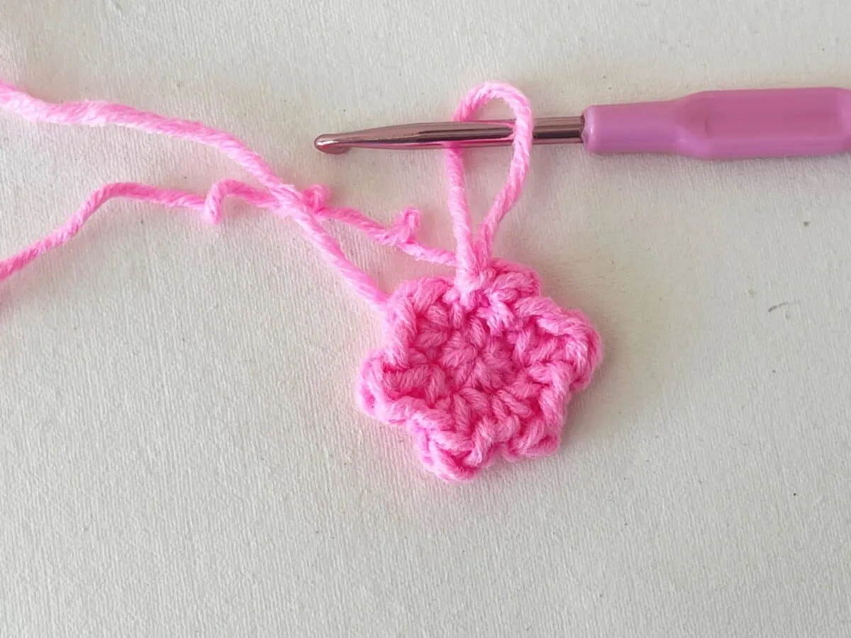 A pink crochet flower with a pink crochet hook.