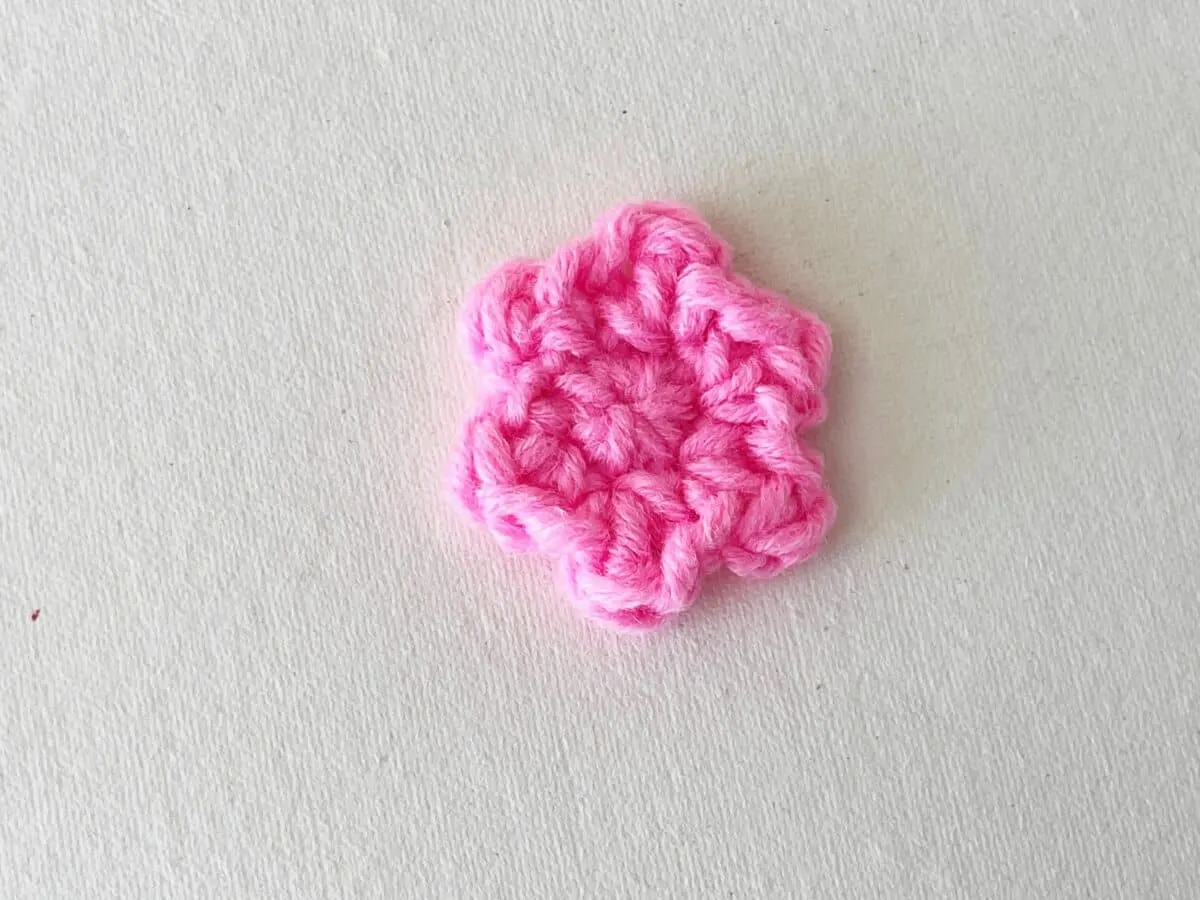 A pink crochet flower on a white surface.