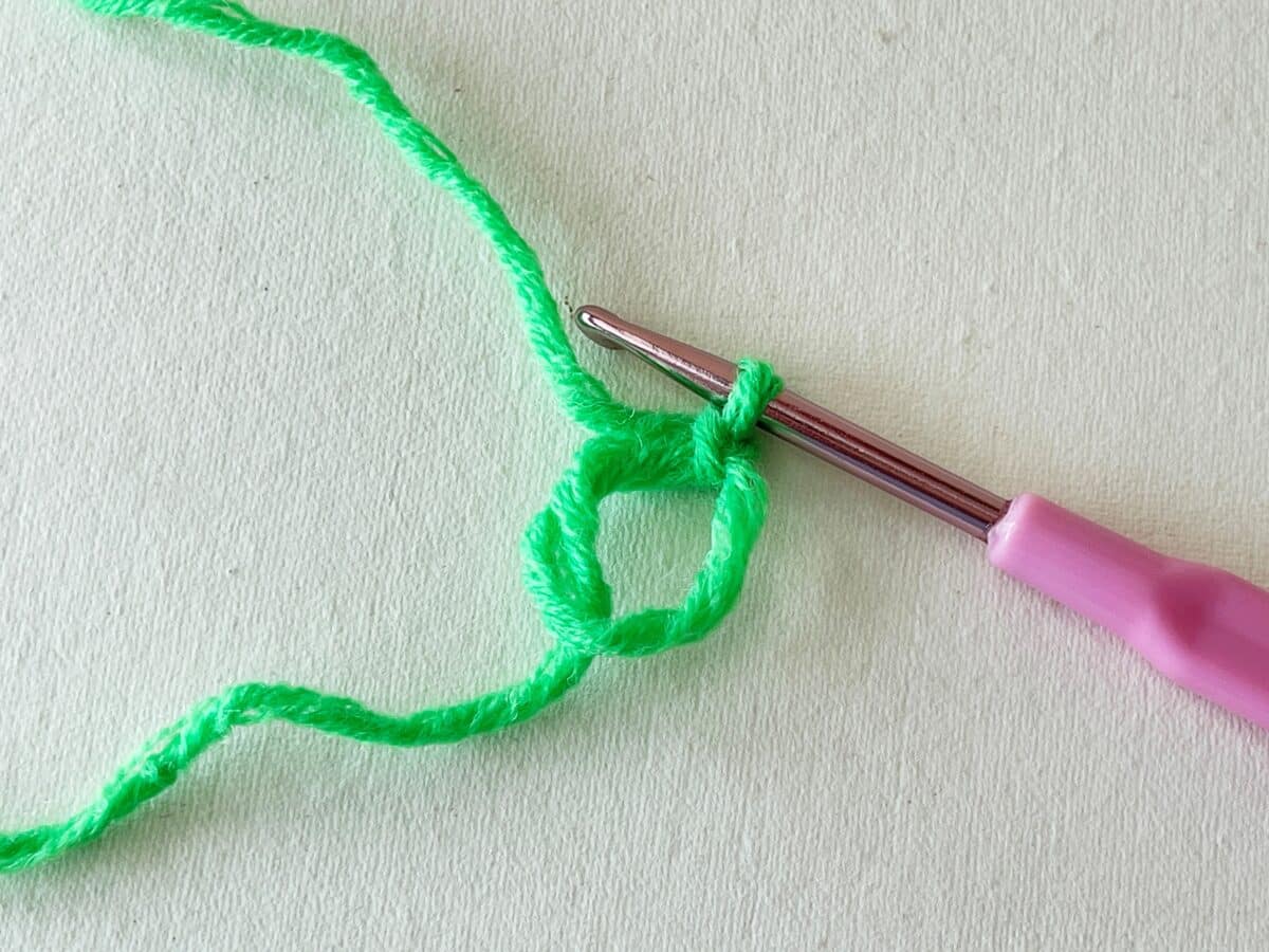 A pink crochet hook is being used to crochet a green yarn.