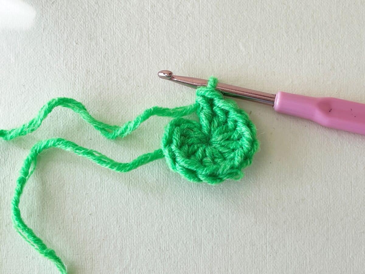 A green crochet stitch with a pink crochet hook.