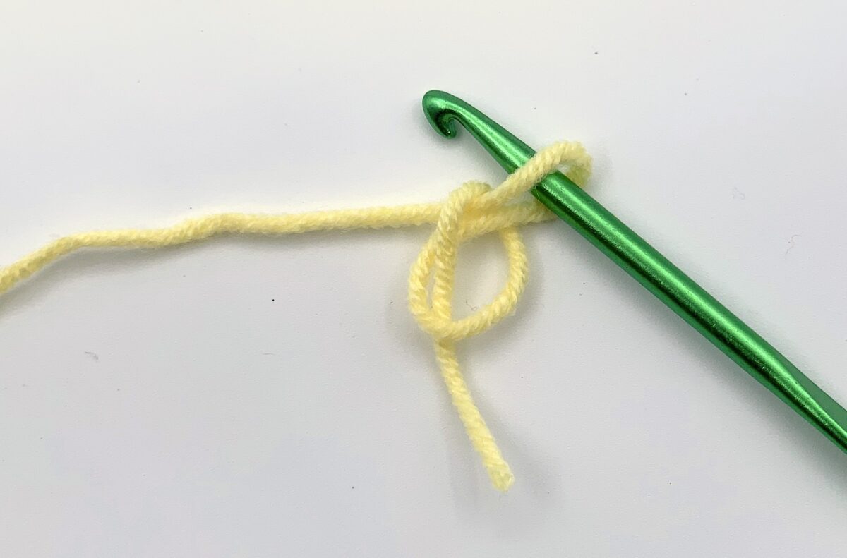 Round 1 - Step 1 A green crochet hook with a yellow yarn.