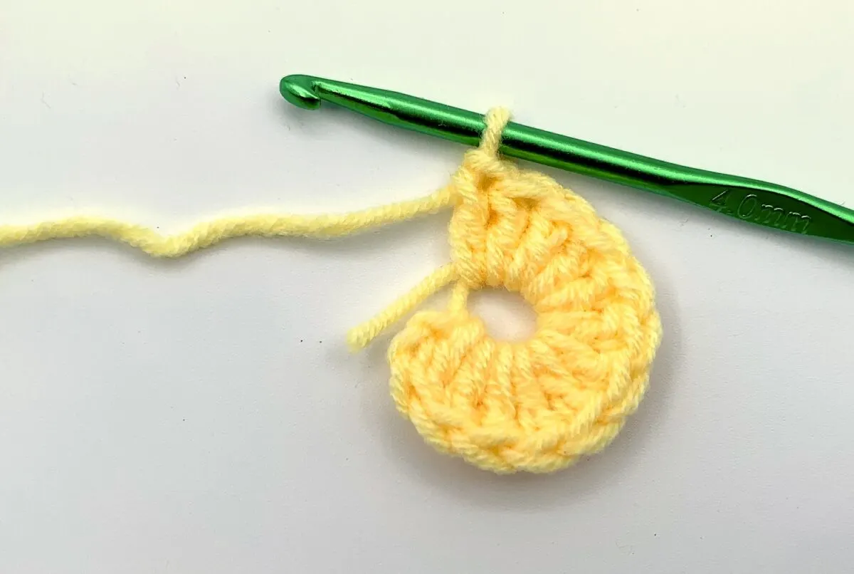Round 1 - Step 2.1 A yellow crocheted stitch with a green crochet hook.