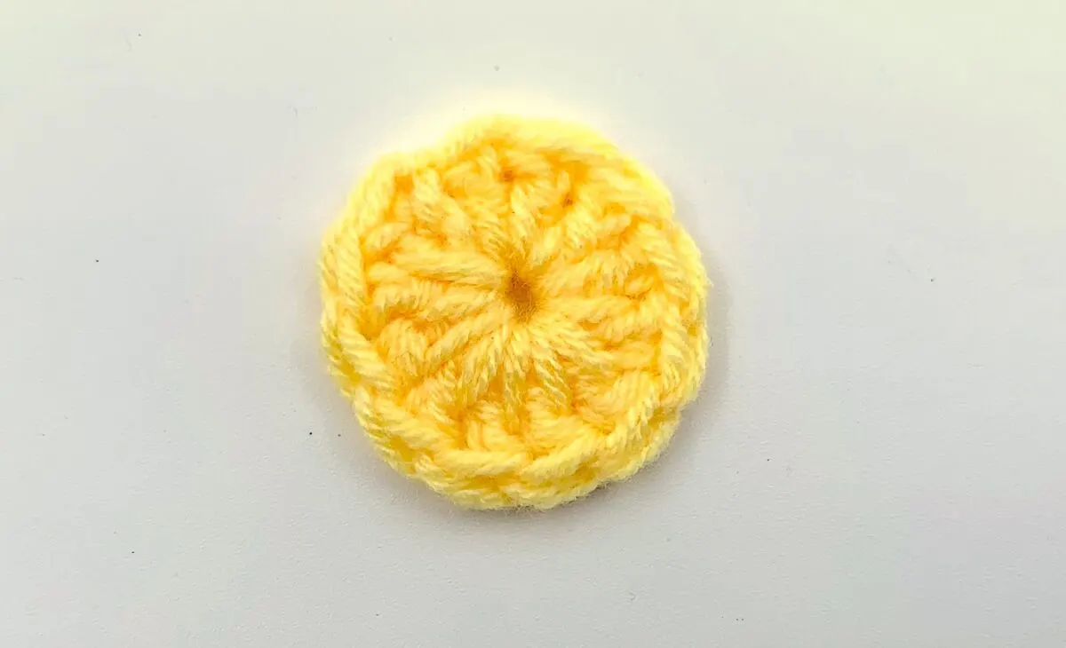 Round 1 - Step 3 A yellow crocheted circle on a white surface.