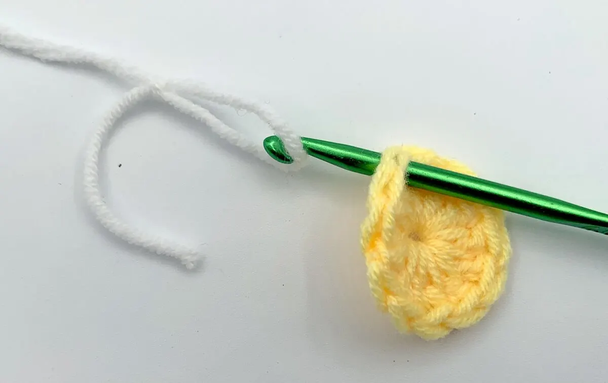 Round 2 - Step 1 A yellow crocheted flower with a green crochet hook.