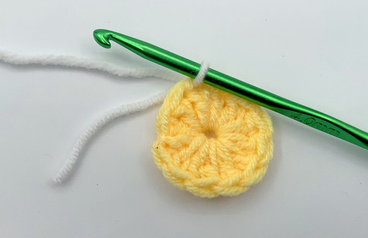 Round 2 - Step 1.1 A yellow crocheted partial flower with a green crochet hook.