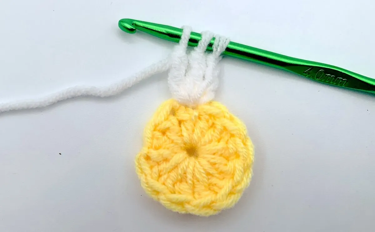 Round 2 - Step 3 A yellow crocheted flower with a green crochet hook.