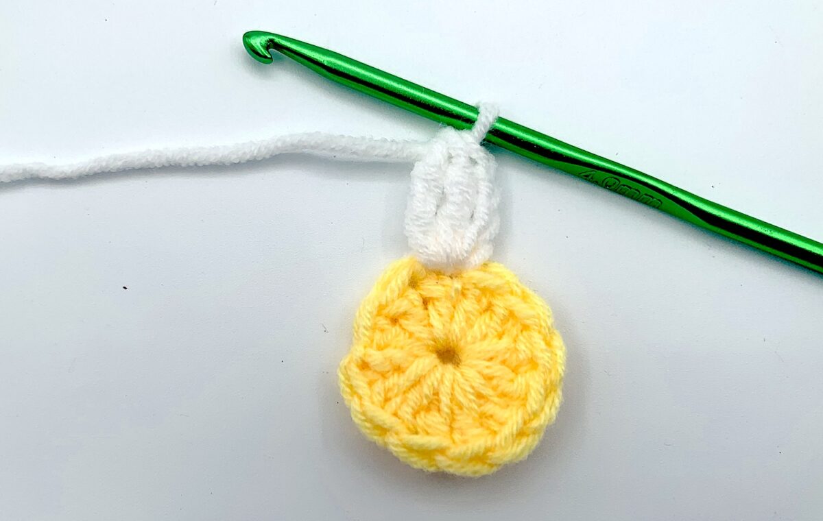 Round 2 - Step 4 A yellow crocheted flower with a green crochet hook.