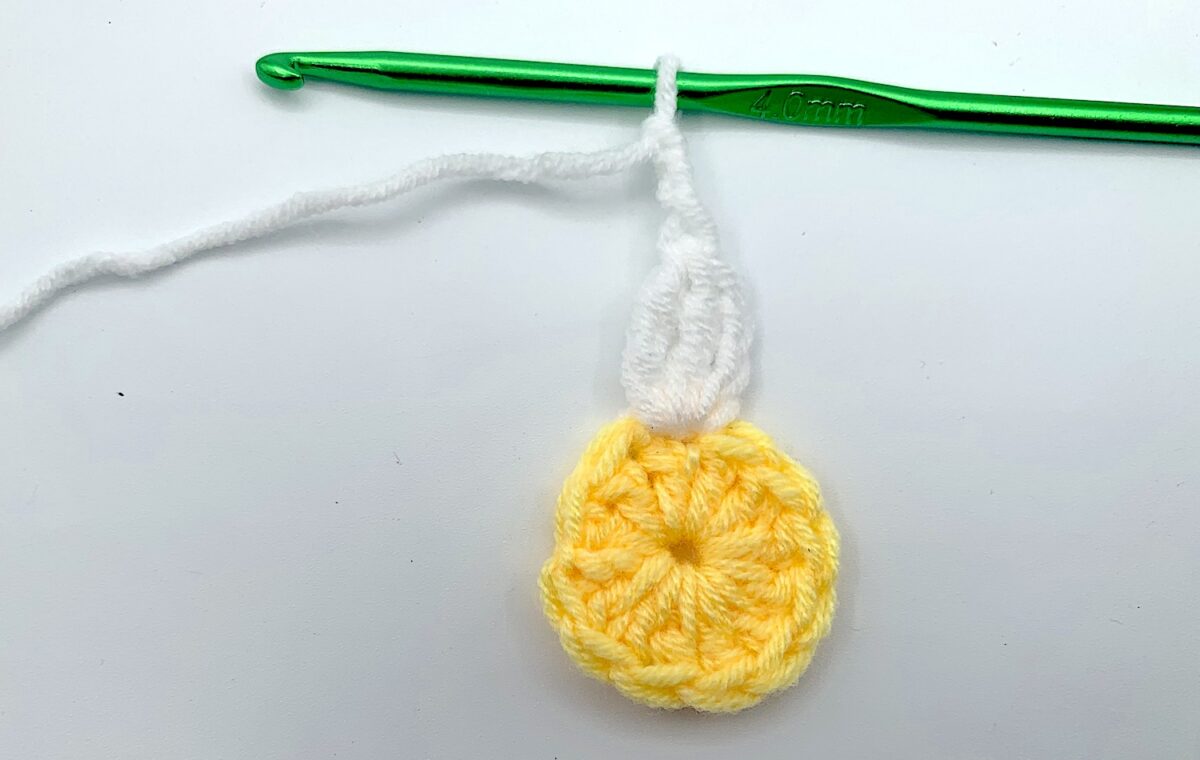 Round 2 - Step 5 A crocheted daisy with a green crochet hook.