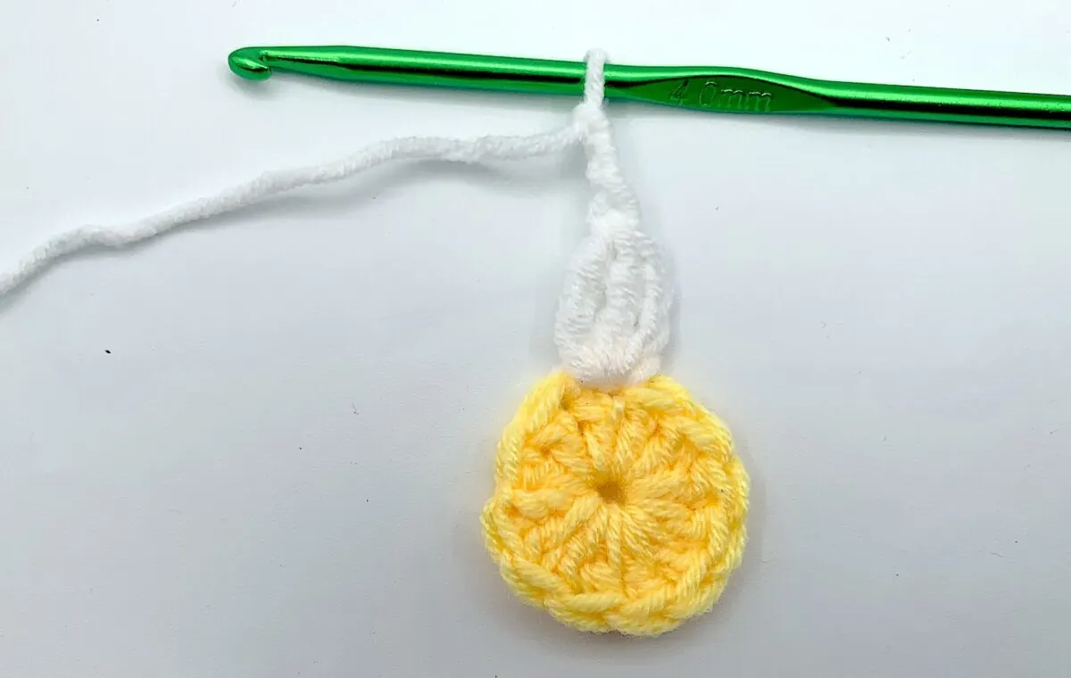 Round 2 - Step 5 A crocheted daisy with a green crochet hook.