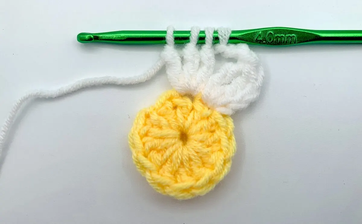 Round 2 - Step 6 A yellow crocheted flower with a green crochet hook.