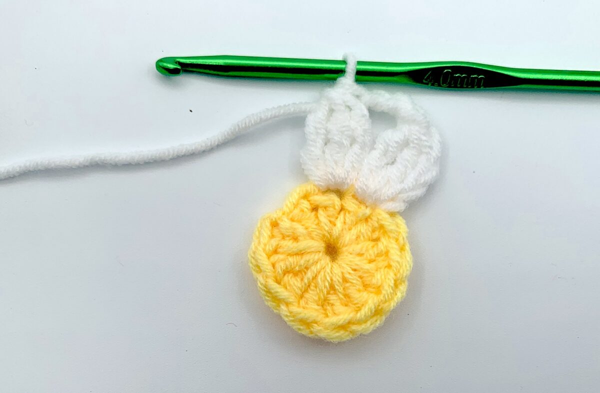 Round 2 - Step 7 A crocheted partial daisy with a green crochet hook.