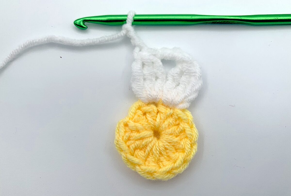 Round 2 - Step 8 A yellow crocheted flower with a green crochet hook.
