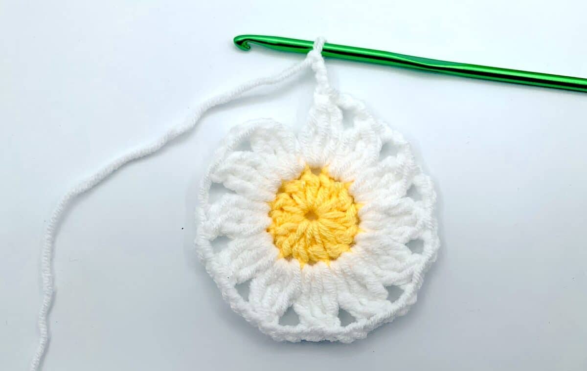 Round 2 - Step 9 A crocheted daisy with a green crochet hook.