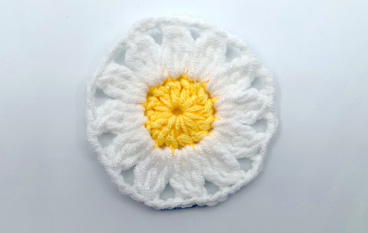 Round 2 - Step 10 A crocheted daisy on a white surface.