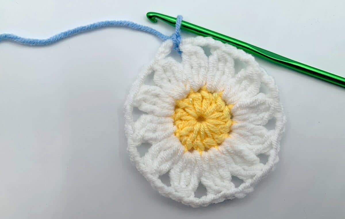 Round 3 - Step 2 A crocheted daisy with a green crochet hook.
