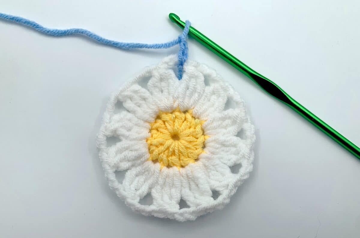Round 3 - Step 2.1 A crocheted daisy with a crochet hook.