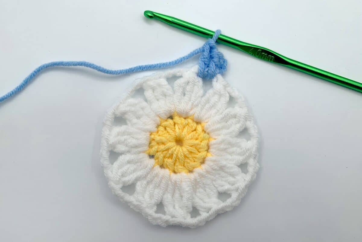 Round 3 - Step 3 A crocheted daisy with a green crochet hook.