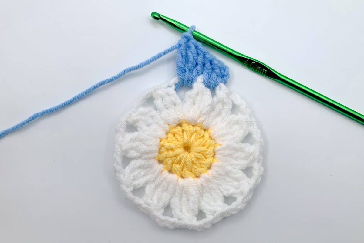 Round 3 - Step 4 A crocheted daisy with a crochet hook.