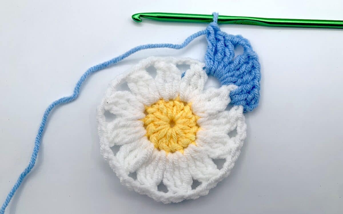Round 3 - Step 6 A crocheted daisy with a crochet hook.