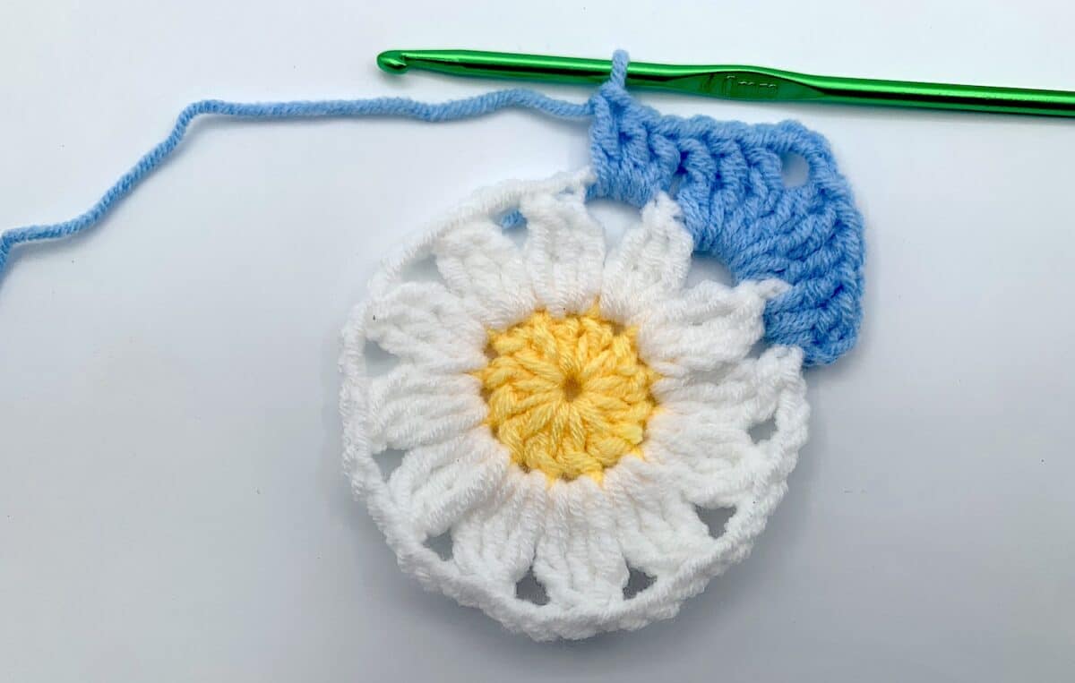 Round 3 - Step 7 A crocheted daisy with a crochet hook.