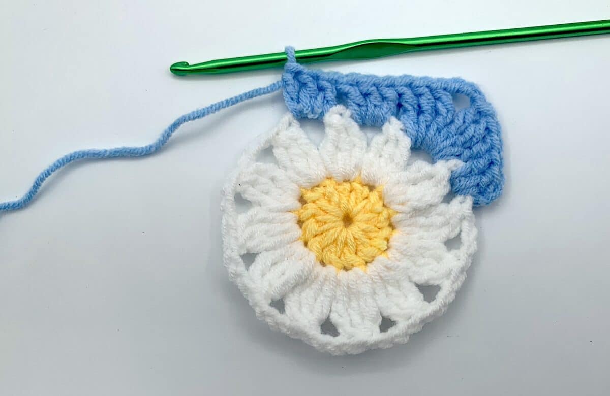 Round 3 - Step 7.1 A crocheted daisy with a crochet hook.