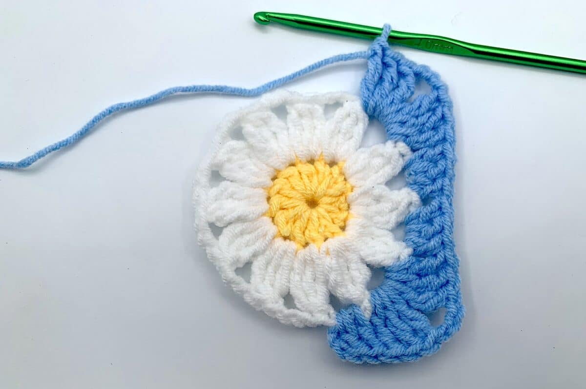 Round 3 - Step 8 A crocheted daisy with a crochet hook.