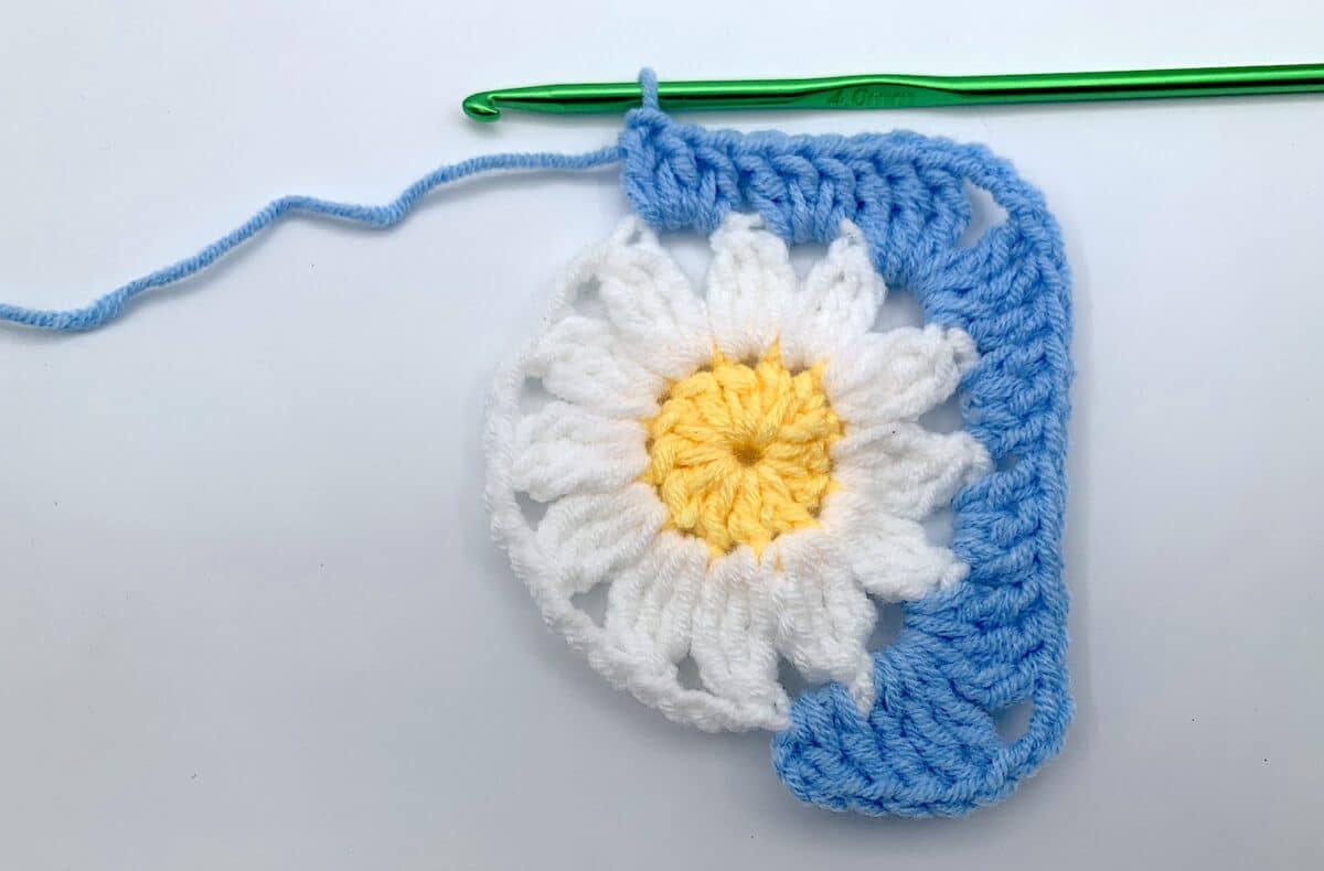 Round 3 - Step 9 A crocheted daisy with a crochet hook.