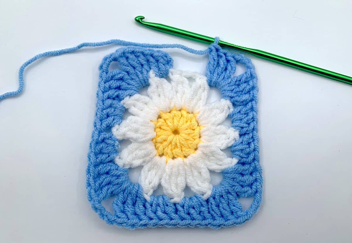 Round 3 - Step 12 A crocheted square with a daisy on it.