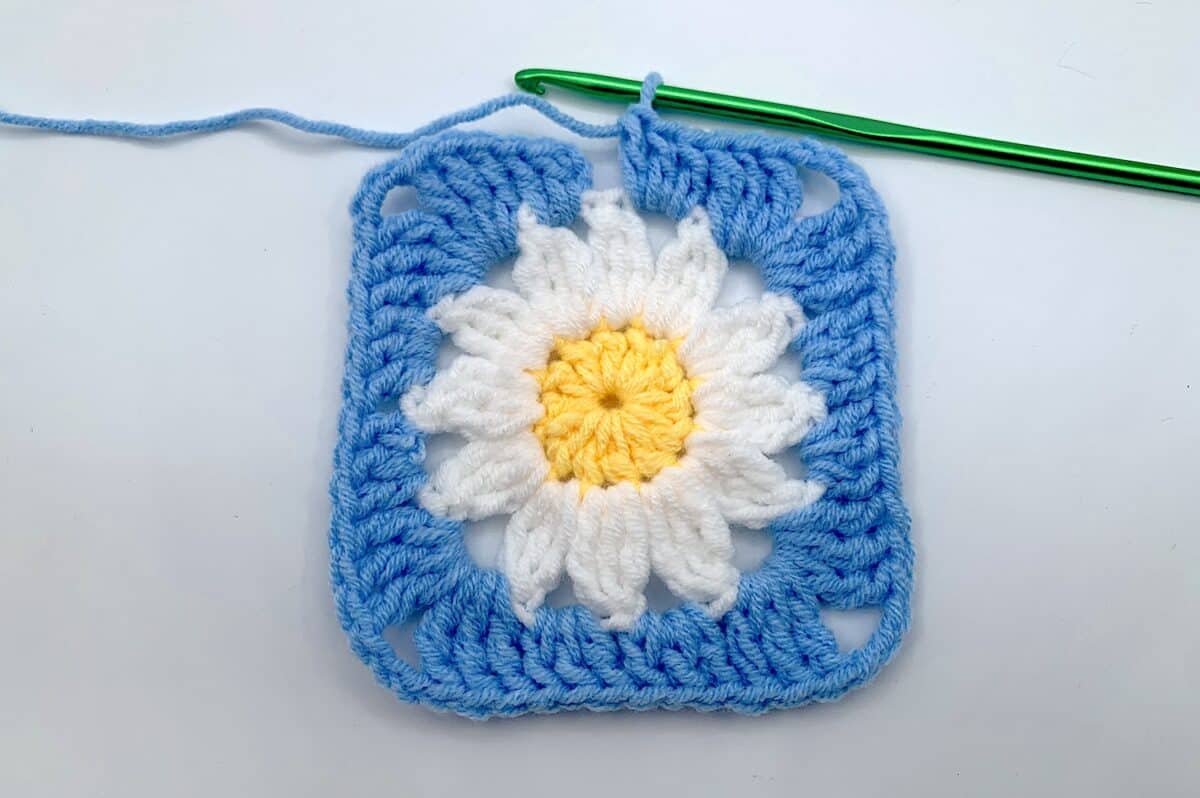Round 3 - Step 13 A crocheted square with a daisy on it.