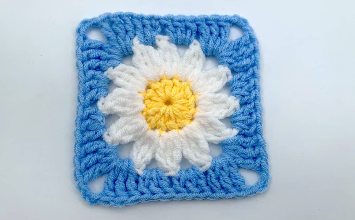 Round 3 - Step 14 A crocheted square with a daisy in the center.