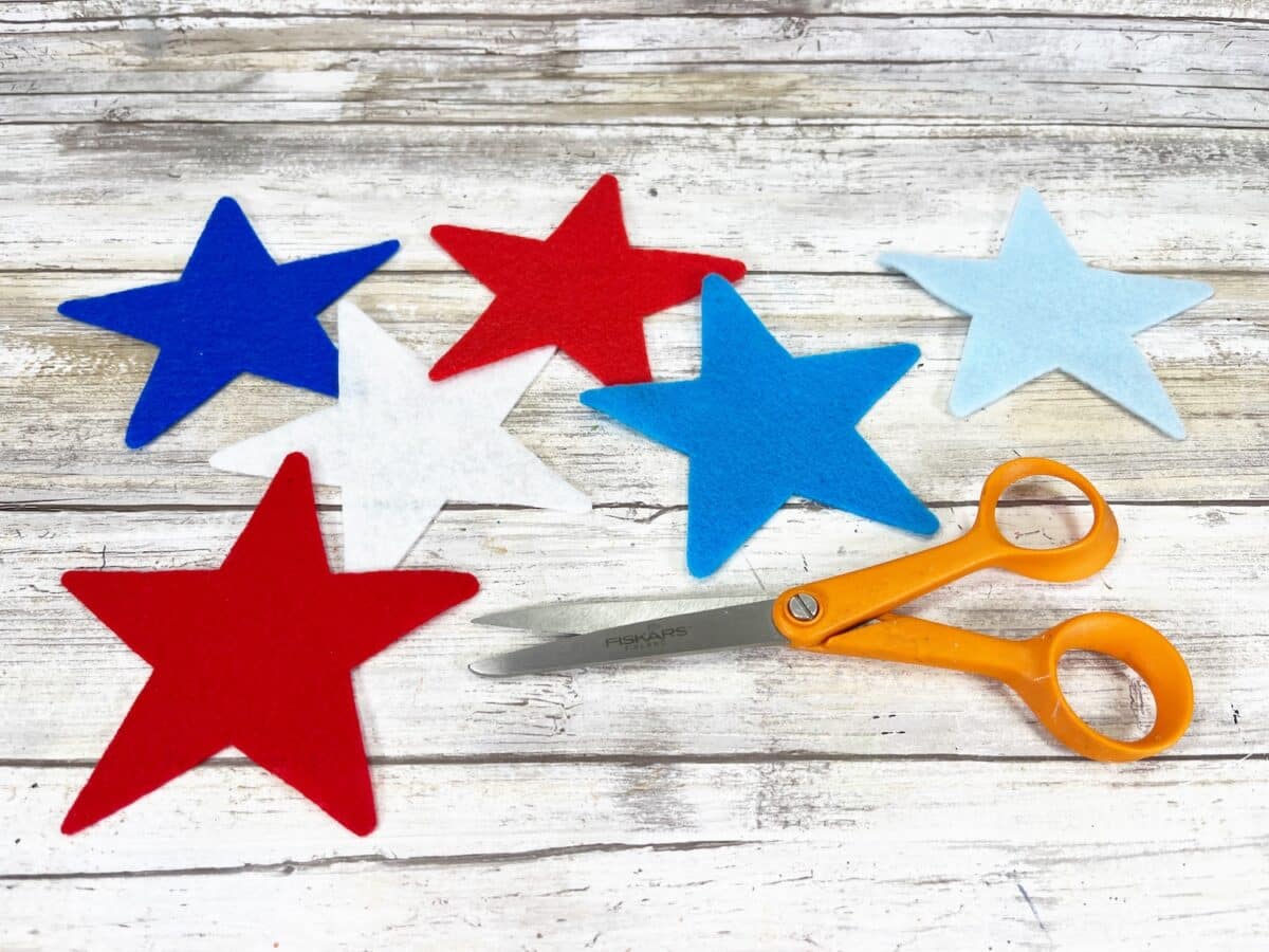 Felt Star People Step 3 Five colorful felt stars and a pair of scissors on a wooden background.