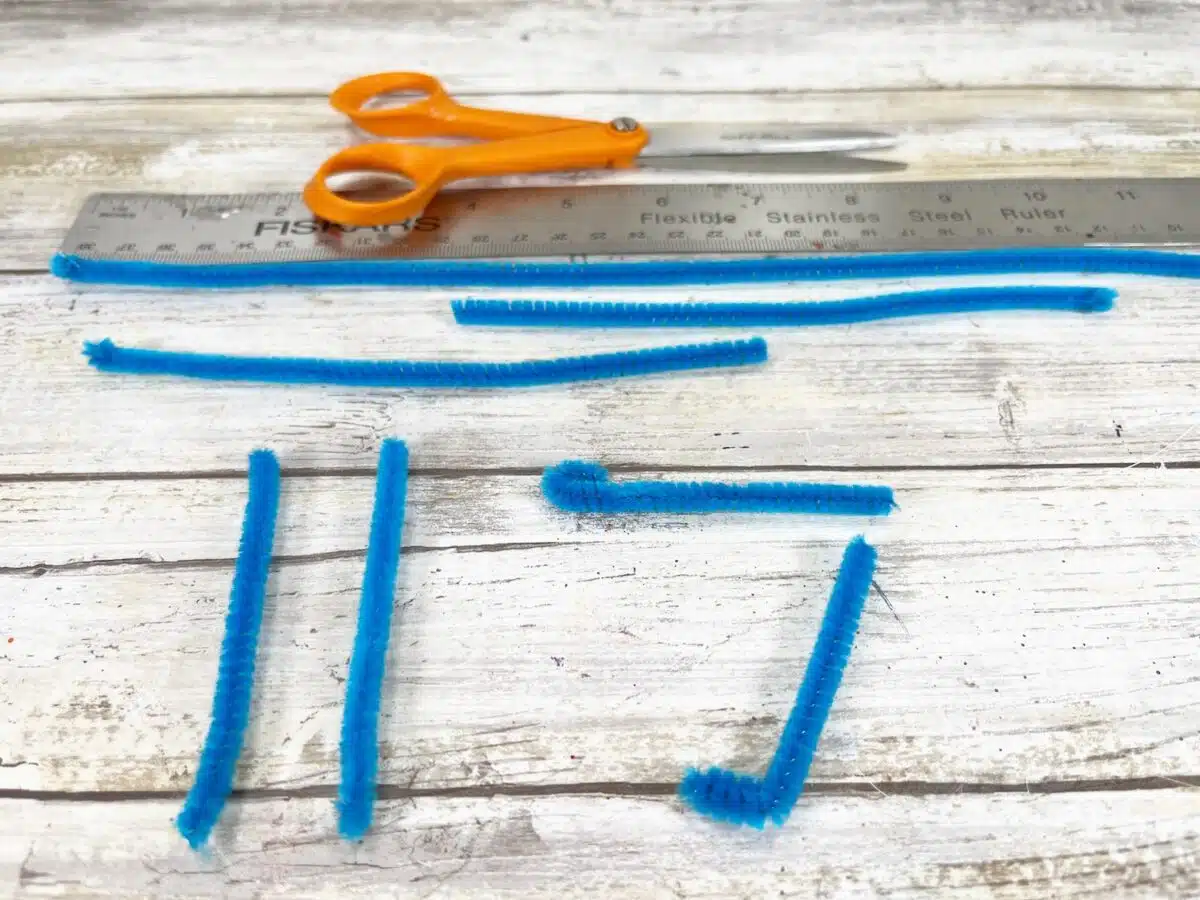 Felt Star People Step 5 Blue pipe cleaners, scissors, and a ruler on a wooden surface.