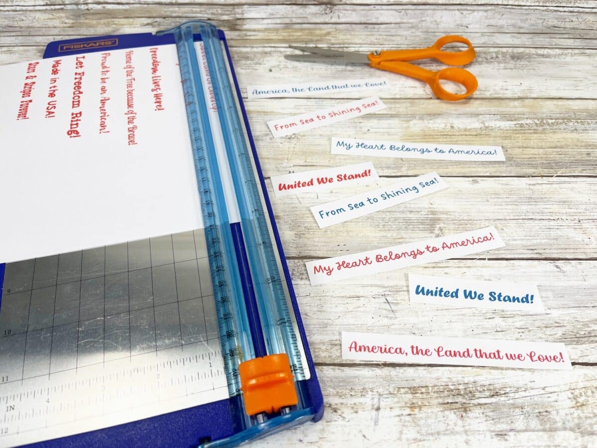 Felt Star People Step 9 A blue three-ring binder open to a page with patriotic phrases, alongside a pair of orange scissors and a steel ruler on a wooden surface.