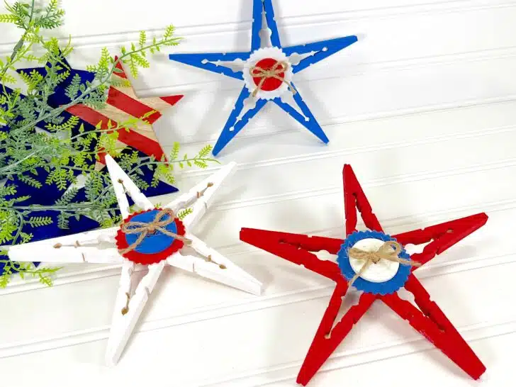 Patriotic Clothespin Stars in red, white, and blue, each adorned with a miniature lifebuoy, against a white wooden background.
