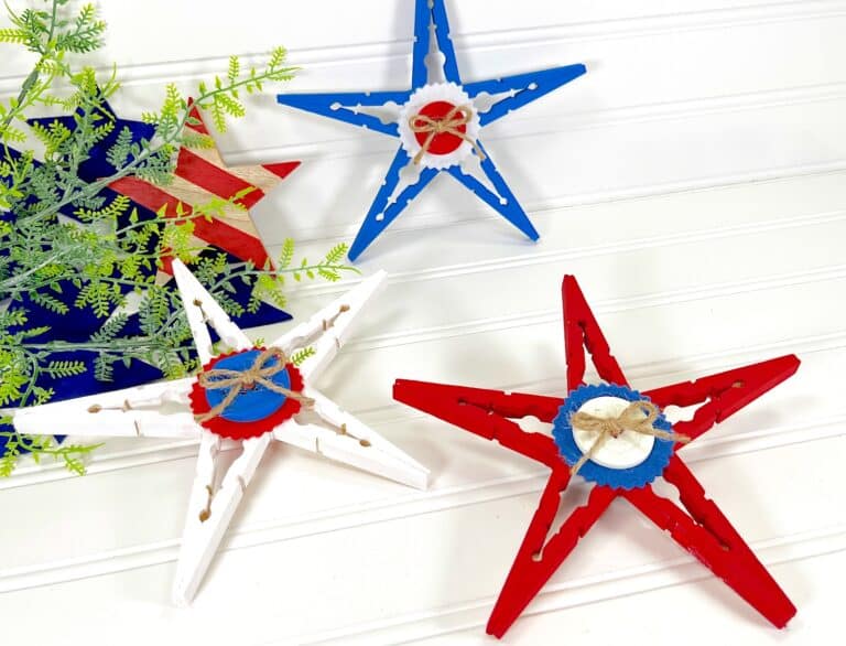 Patriotic Clothespin Stars in red, white, and blue, each adorned with a miniature lifebuoy, against a white wooden background.