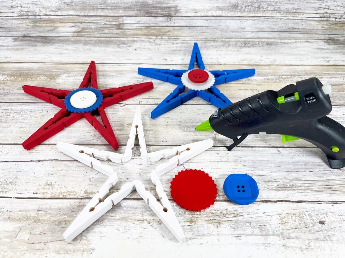 Patriotic Clothespin Stars Step 7 A hot glue gun surrounded by colorful diy fidget spinners made from clothespins and buttons on a wooden surface.