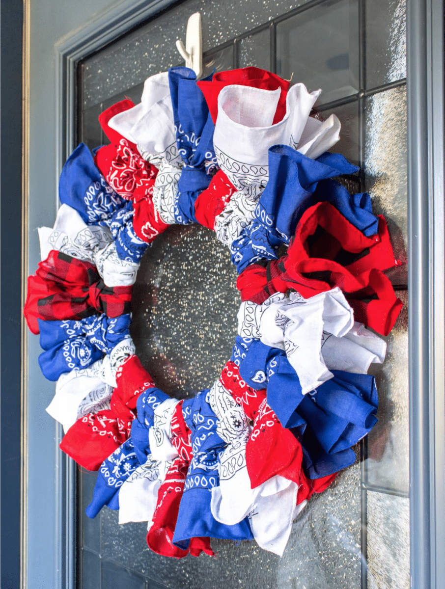 A Fourth of July wreath made of red, white, and blue bandanas hangs on a glass-paneled door.