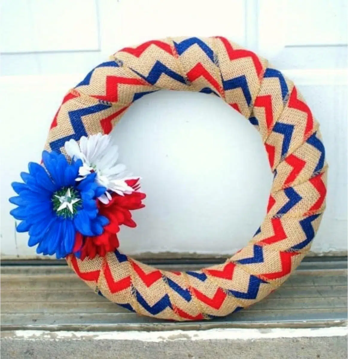 A Fourth of July decorative wreath featuring a red, blue, and beige chevron pattern and adorned with red, white, and blue flowers.