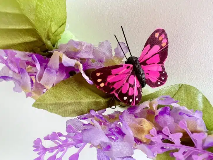 A decorative pink and black butterfly perched on artificial purple flowers.