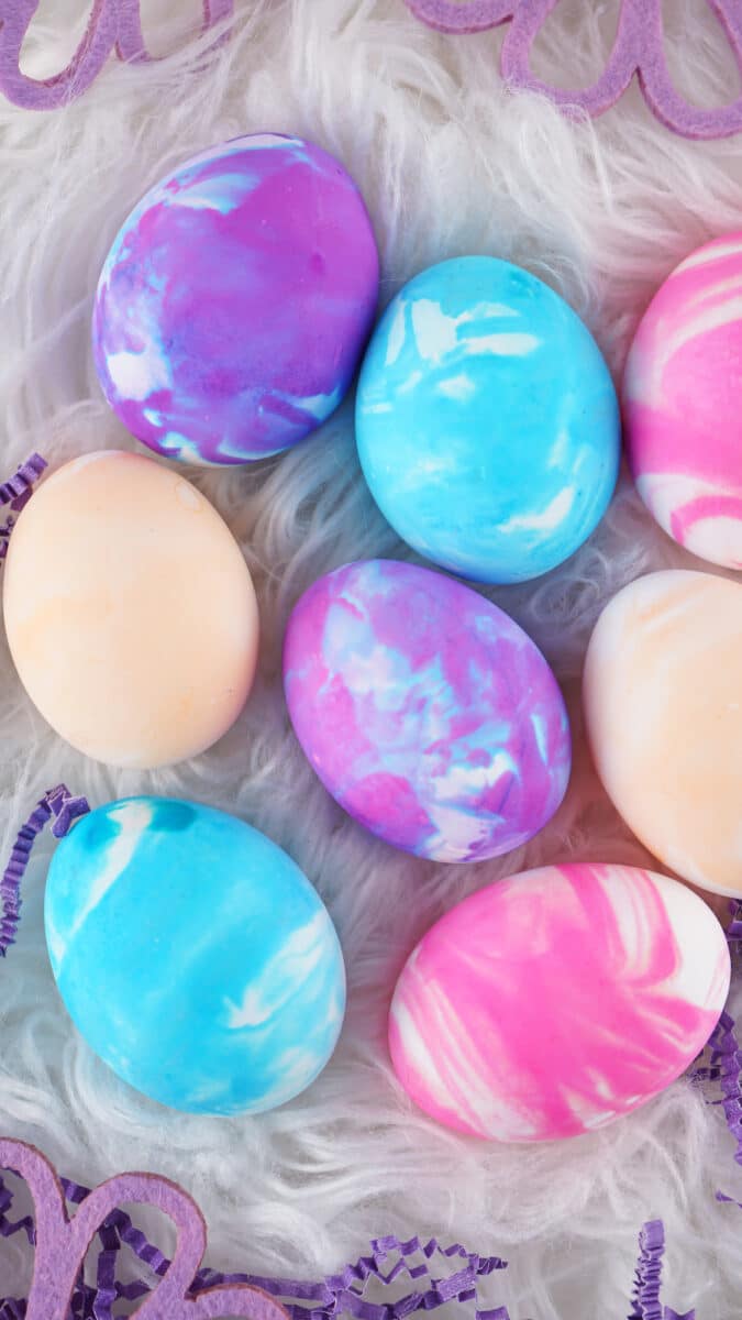 Colorful marbled Cool Whip eggs arranged on a fluffy white background with purple decorations.