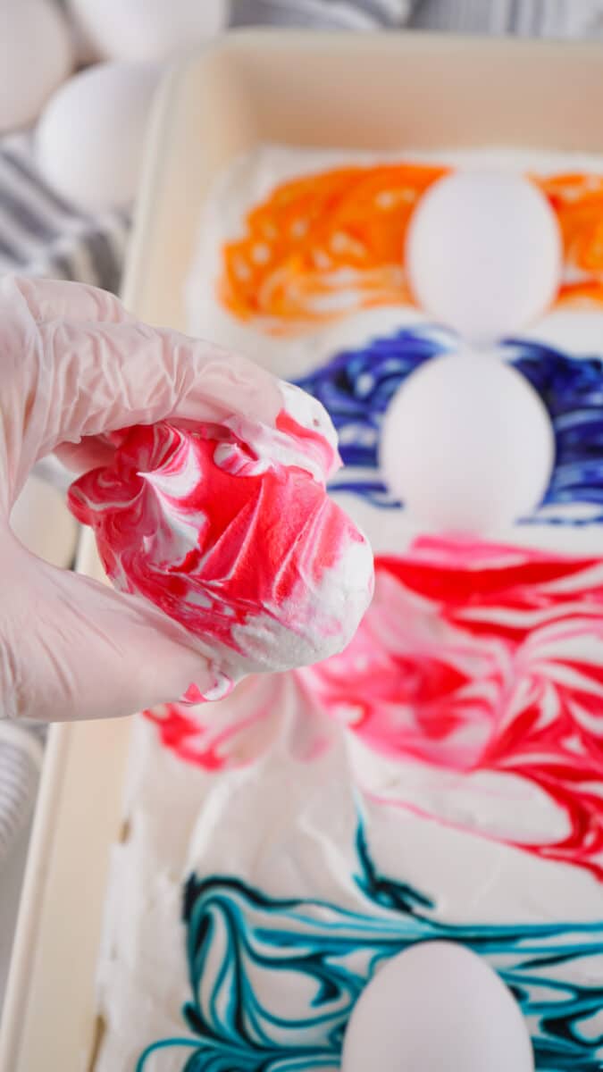Person dyeing an egg with swirls of red and white color for Easter decoration using Cool Whip.