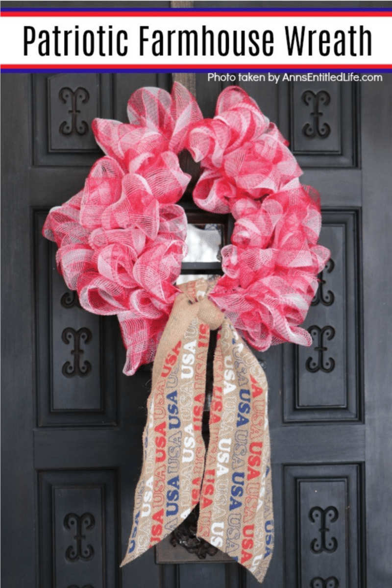 A red mesh wreath with a patriotic ribbon displayed on a black double door.