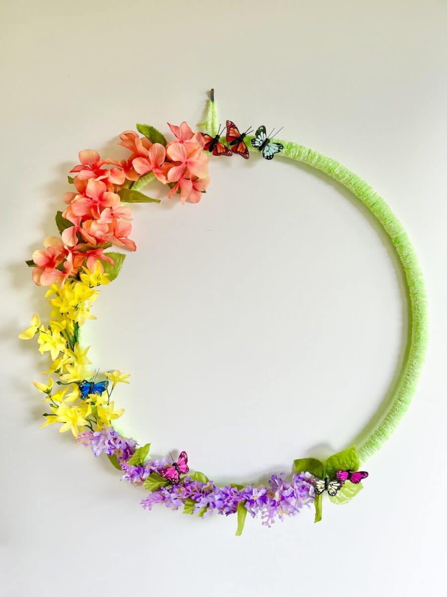 Circular floral wreath with colorful fake flowers and butterfly decorations against a plain background.