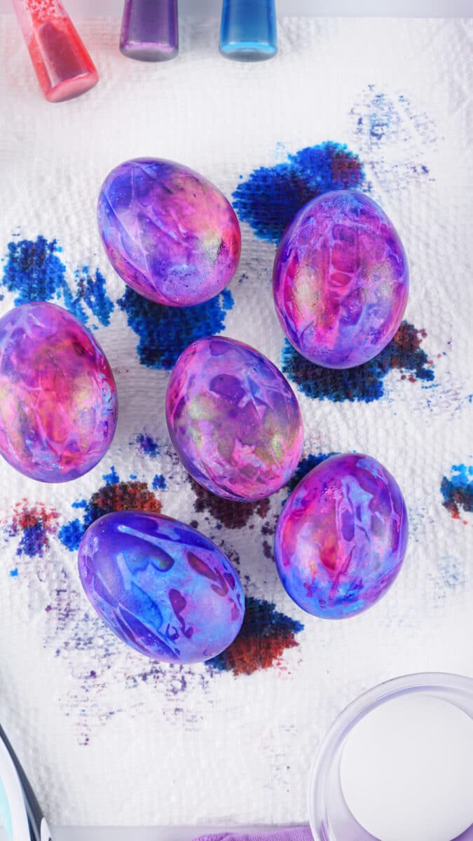 Colorful galaxy dyed easter eggs surrounded by dyeing materials on a white background.