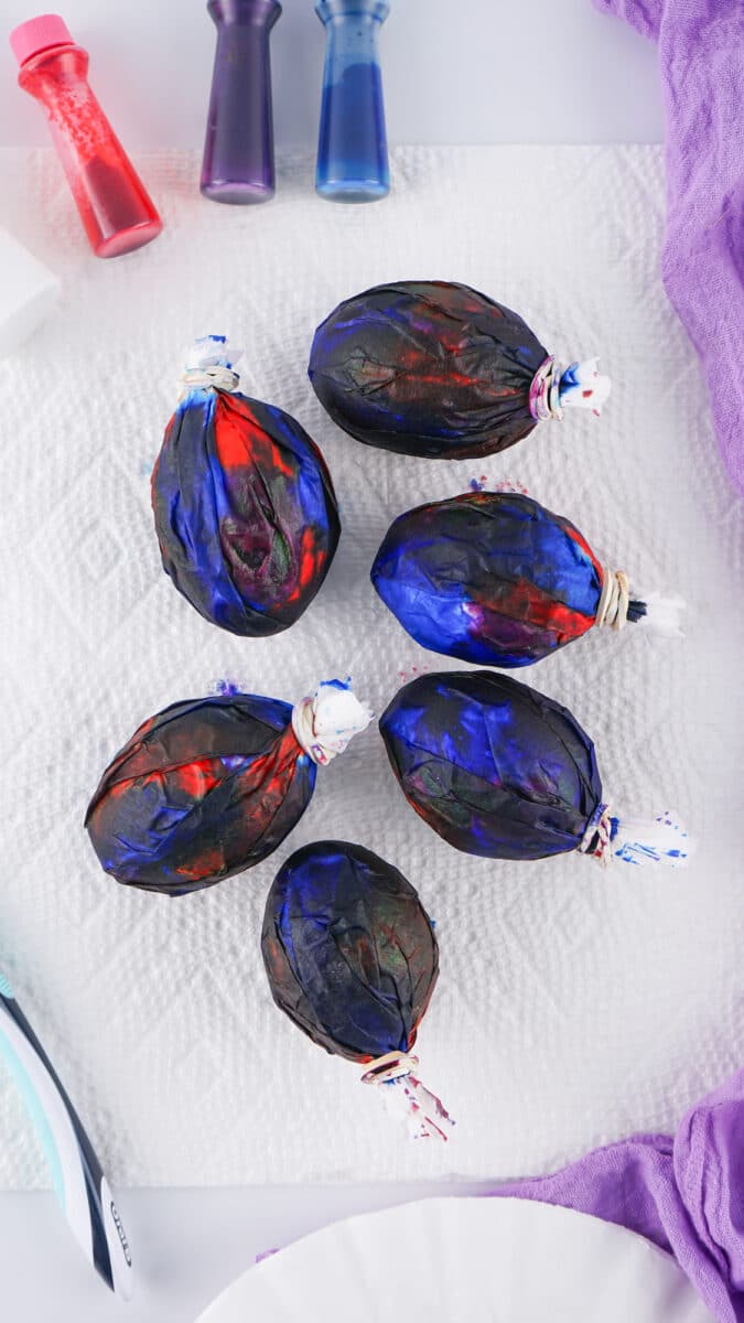 Hand-painted galaxy easter eggs in vibrant blues and reds, displayed on a white surface with colorful fabrics.