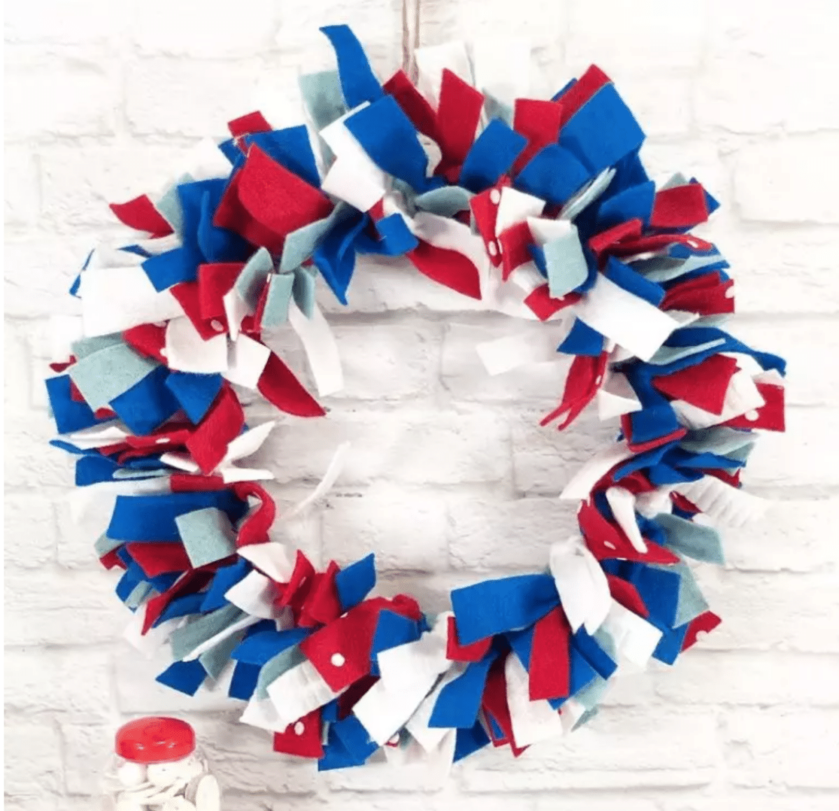 A Fourth of July red, white, and blue fabric wreath against a white brick wall background.