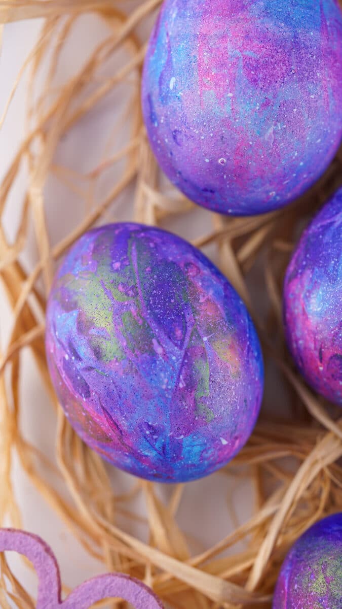 Galaxy-themed easter eggs nestled in straw with a hint of a galaxy decorative element in the foreground.