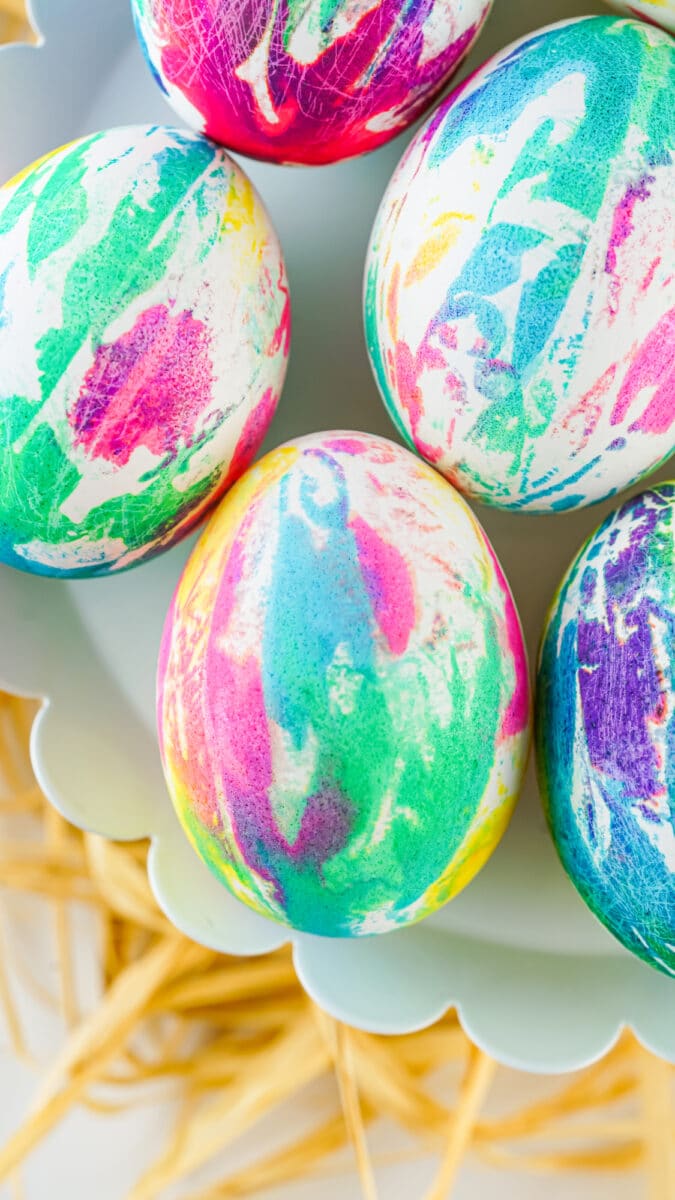 Colorfully tie-dye Easter eggs resting on a pale blue egg tray.